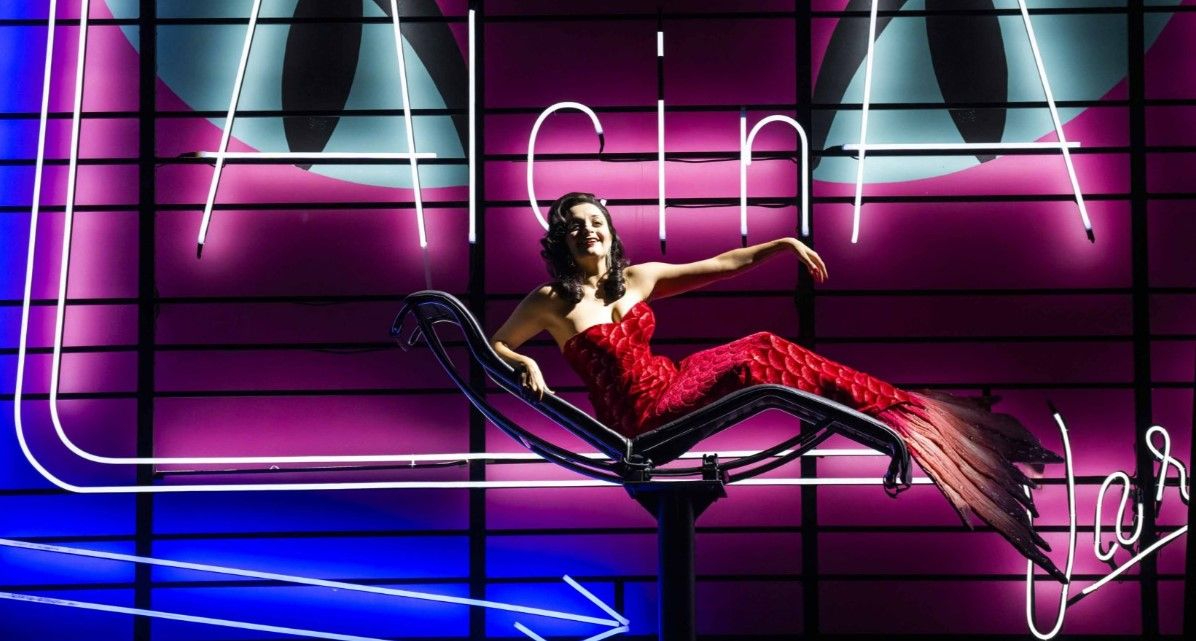 Alcina Playbill - female actor in evening dress on modern couch